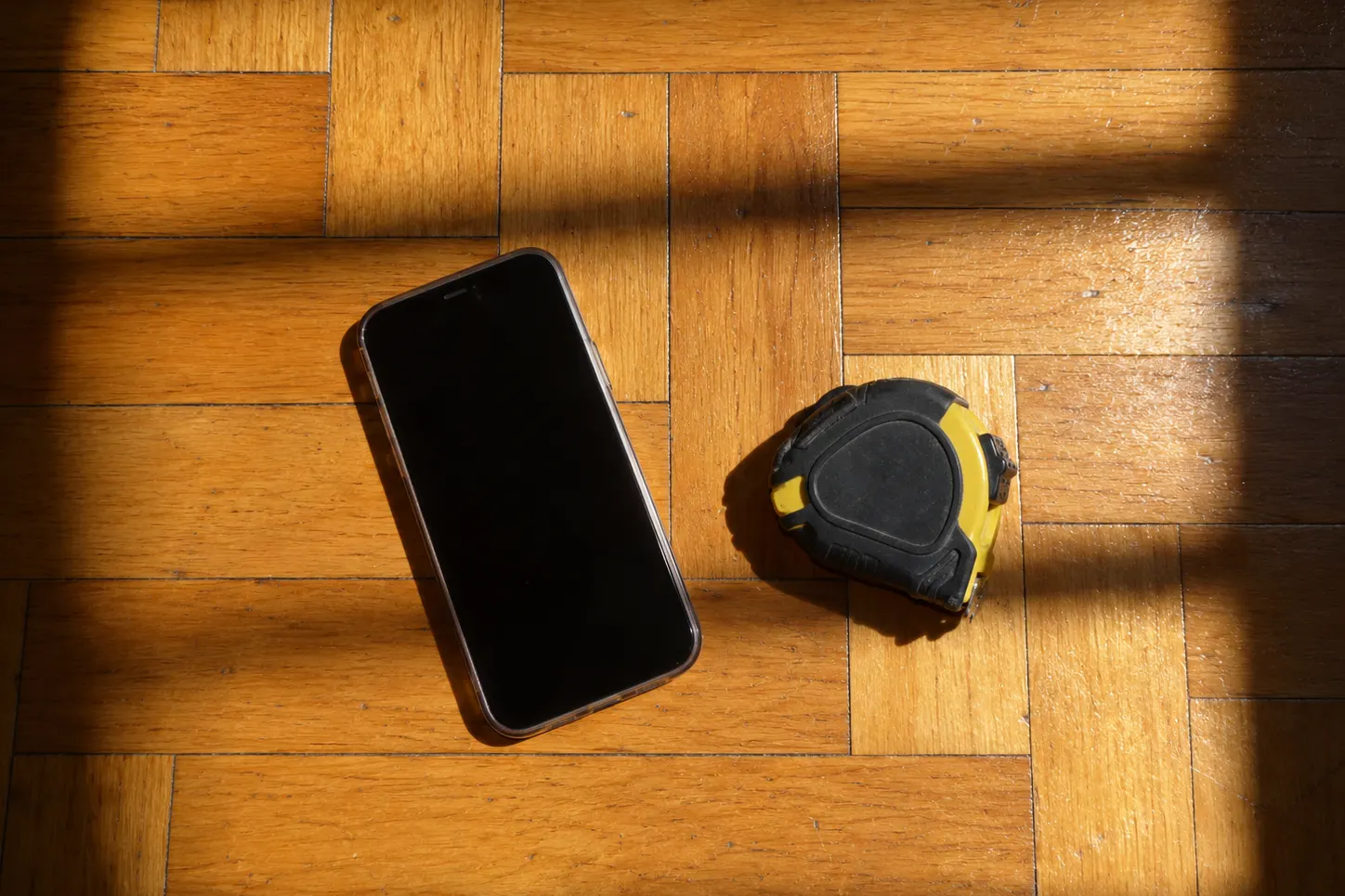 Celular y cinta métrica sobre un piso de parquet