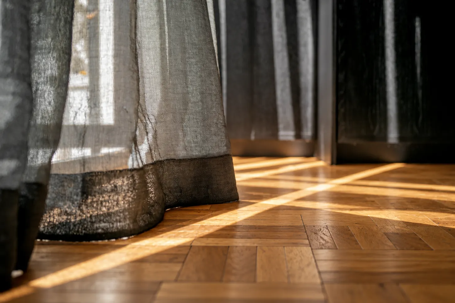 Sol que entra por la cortina sobre un piso de parquet